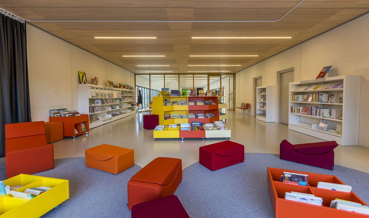Bright library reading room with colorful seating and bookshelves, illuminated by Artemide recessed linear ceiling lights