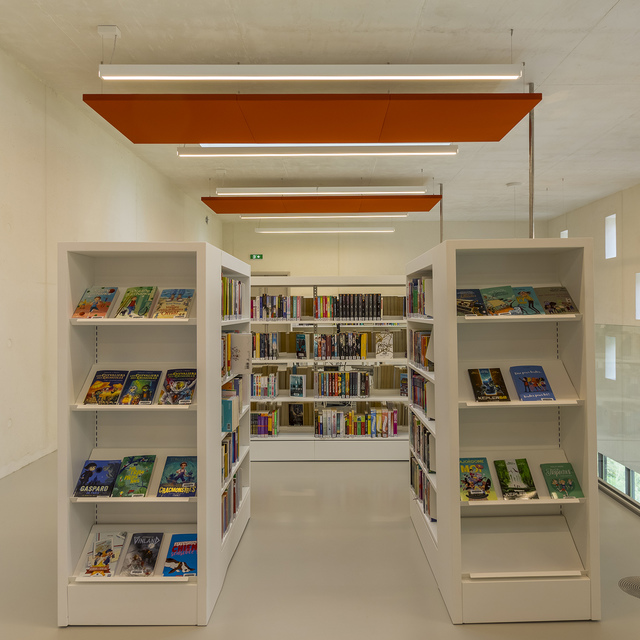 Library interior with white bookshelves and linear pendant lights beneath orange acoustic panels on the ceiling.