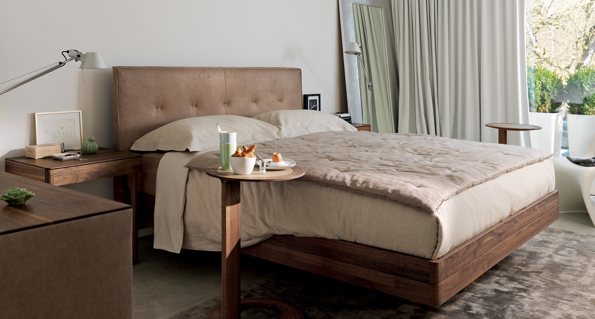 Elegant bedroom with walnut wood bed, beige upholstered headboard, neutral bedding, and an Artemide adjustable desk lamp on the nightstand