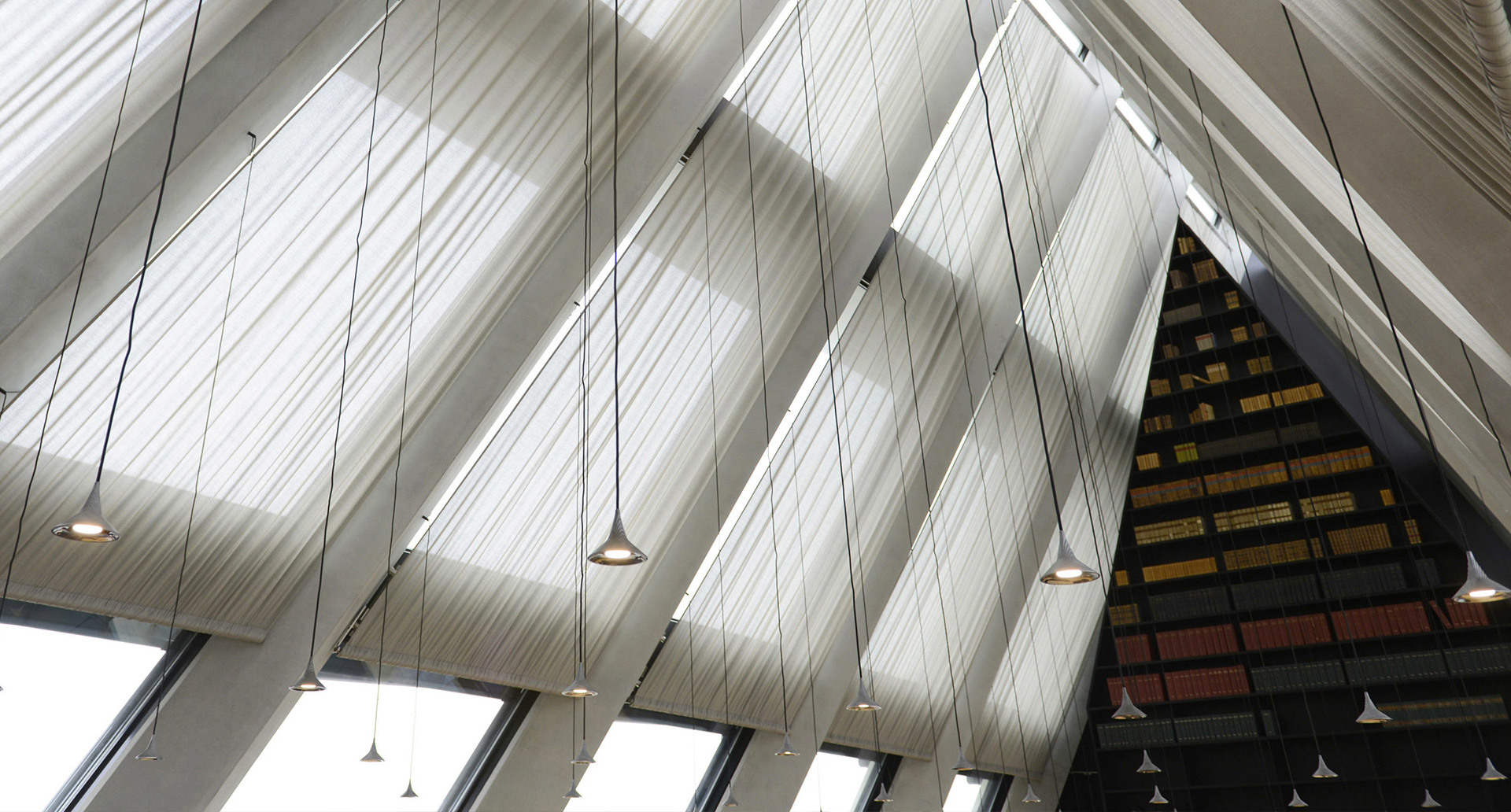 Interior ceiling with dramatic diagonal white fabric panels and multiple small pendant lights hanging on thin cables in a modern building.