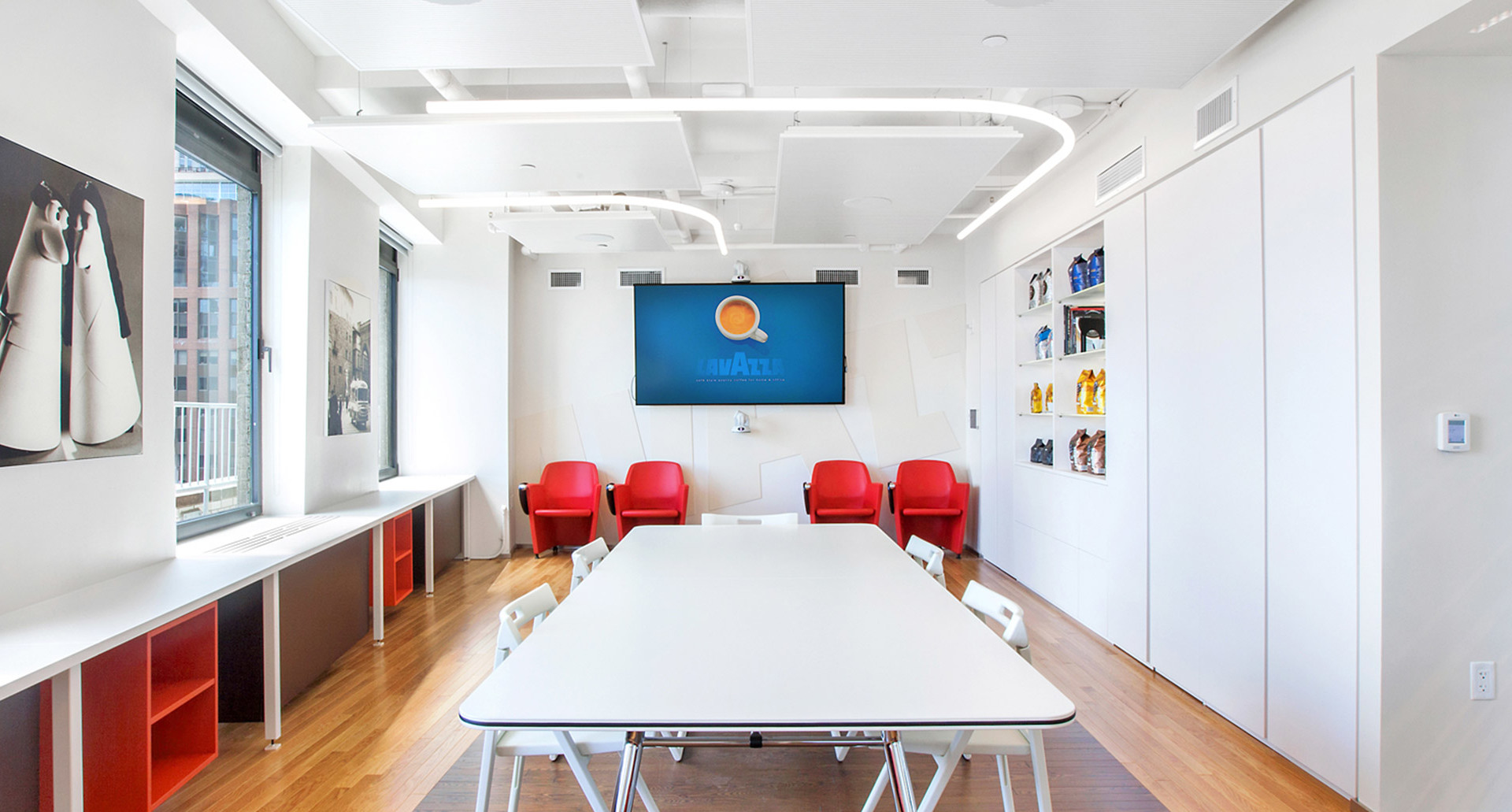 Modern conference room with Artemide curved LED ceiling light, white table, red chairs, and presentation screen on white wall.