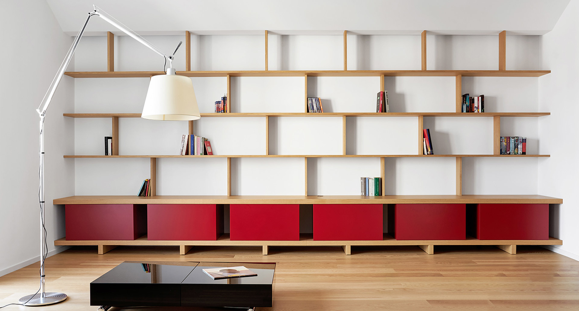 Artemide Tolomeo Mega floor lamp with white shade illuminating a modern living room with large wooden shelving unit and red cabinets