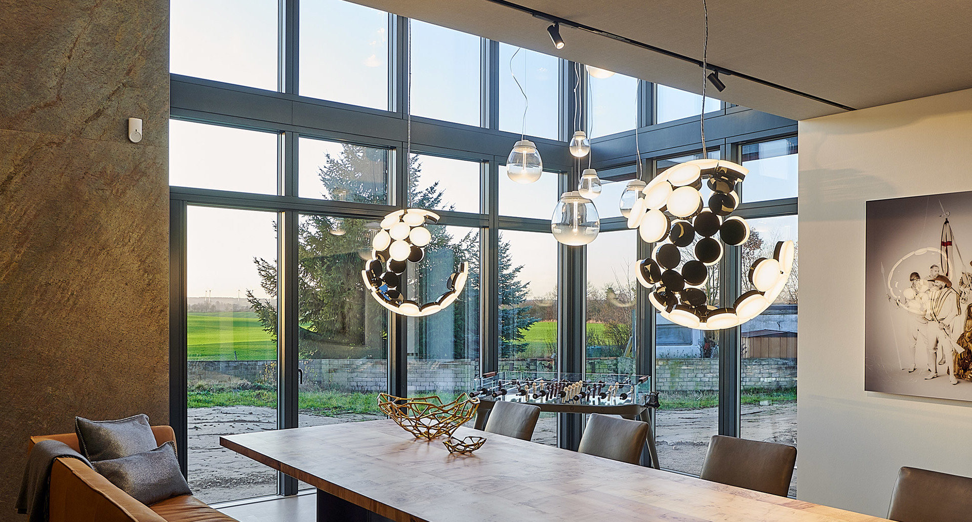 Dining room with large windows and three Artemide pendant lights featuring circular black and white LED clusters over a wooden table.