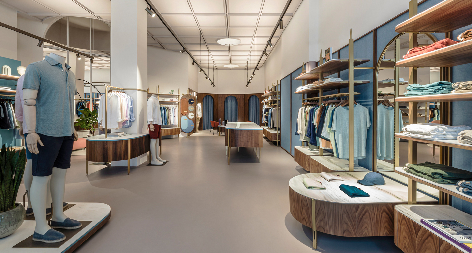 Modern menswear boutique interior with track lighting and recessed ceiling fixtures illuminating clothing displays and wooden shelving units.