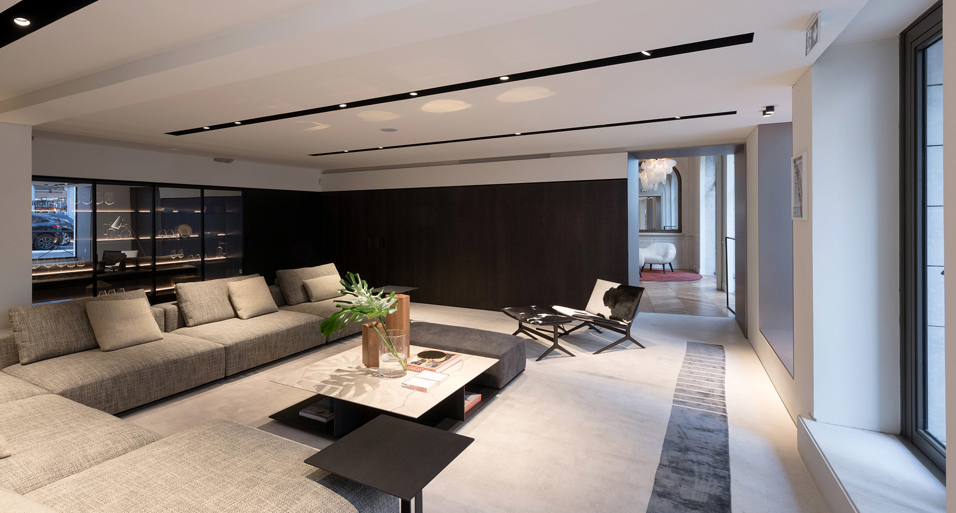 Modern living room with recessed ceiling spotlights, large grey sofa, black coffee table, and sleek minimalist design with dark accent wall.