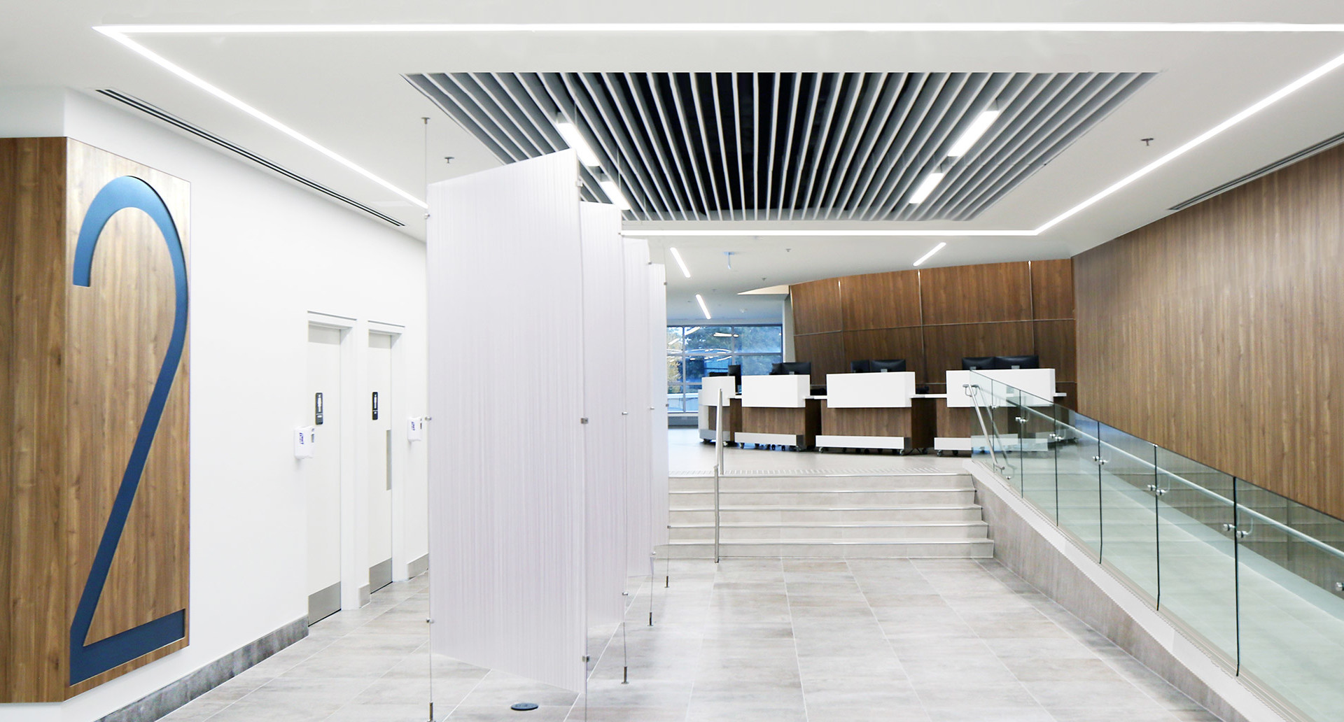 Modern office lobby with recessed linear LED ceiling lights illuminating white walls, marble floors, wood panels, and a reception area.