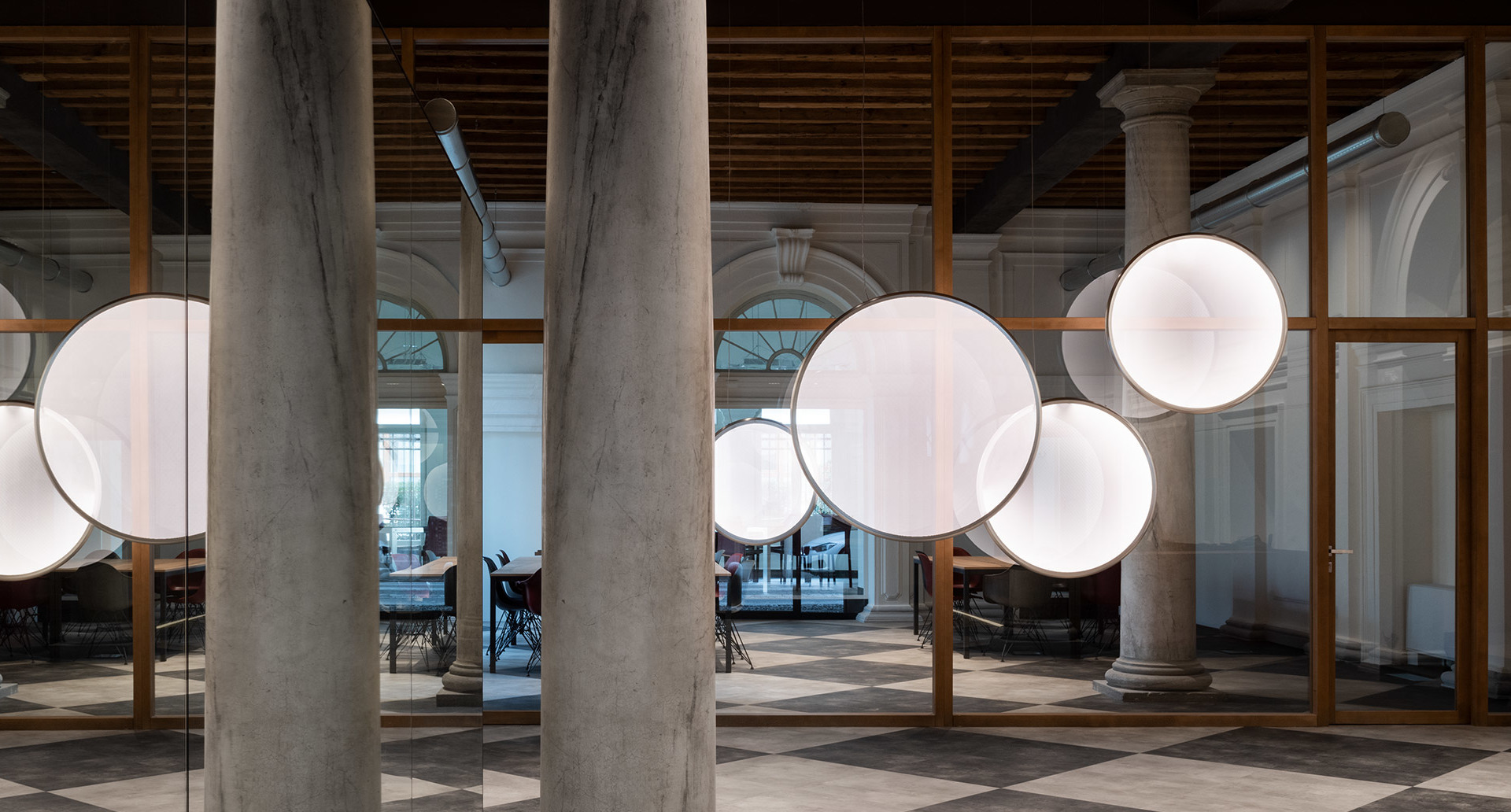 Multiple large glowing spherical pendant lights suspended among marble columns in an elegant historic interior space.