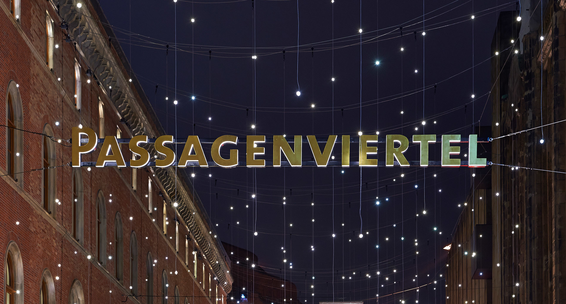 Night view of Passagenviertel street with illuminated sign and strings of small white lights suspended between historic brick buildings