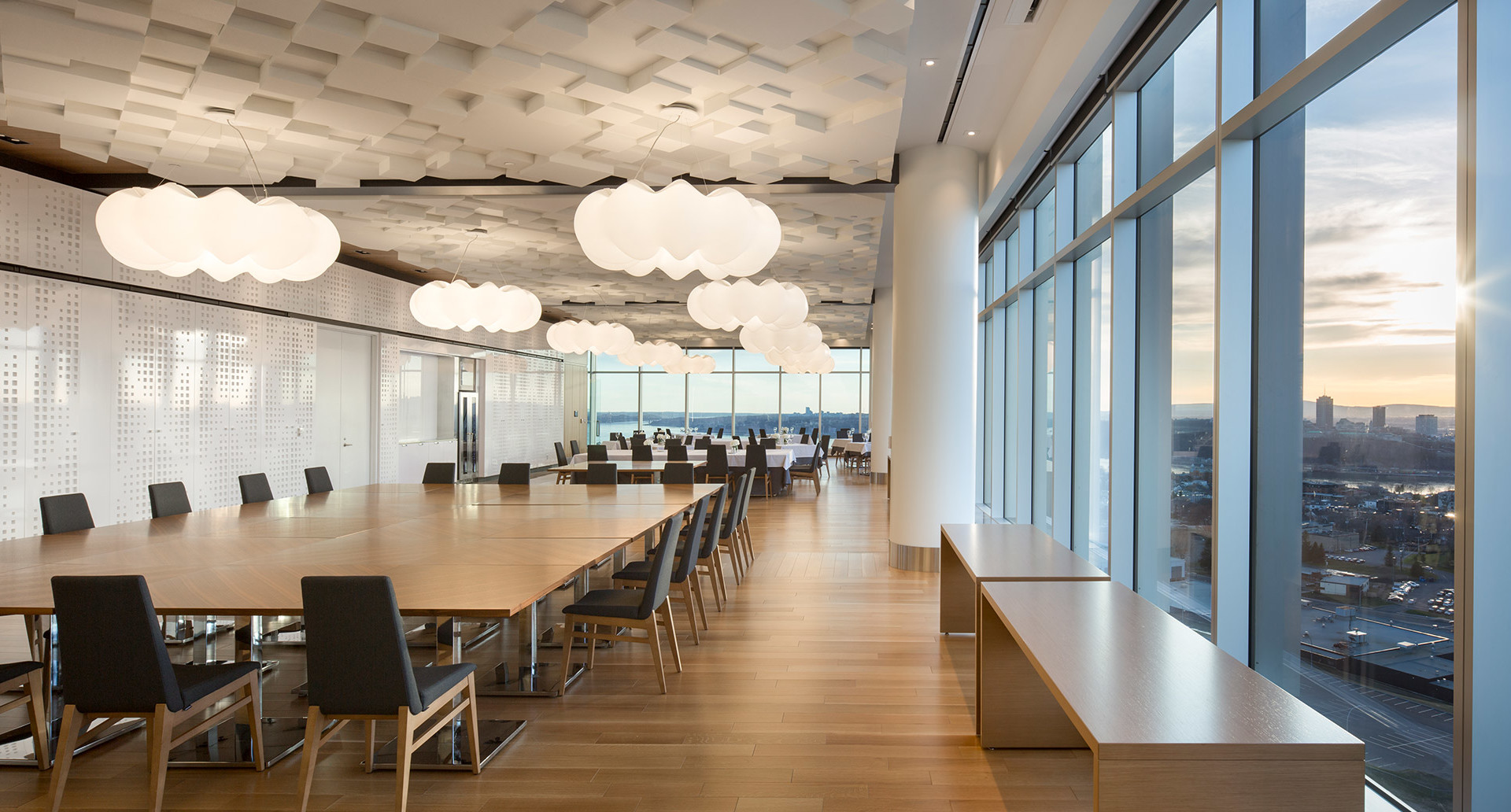 Modern conference dining room with Artemide cloud-shaped white pendant lights hanging from textured ceiling, floor-to-ceiling windows, city view at sunset