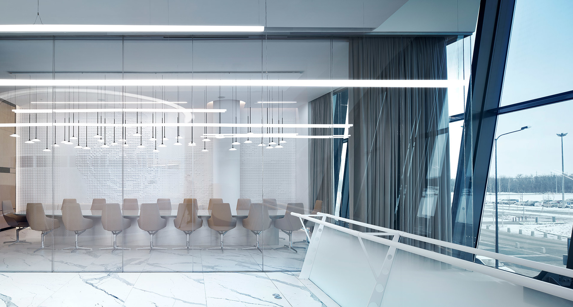 Modern conference room with marble floors, glass walls, and linear pendant lights illuminating a long table with beige chairs.