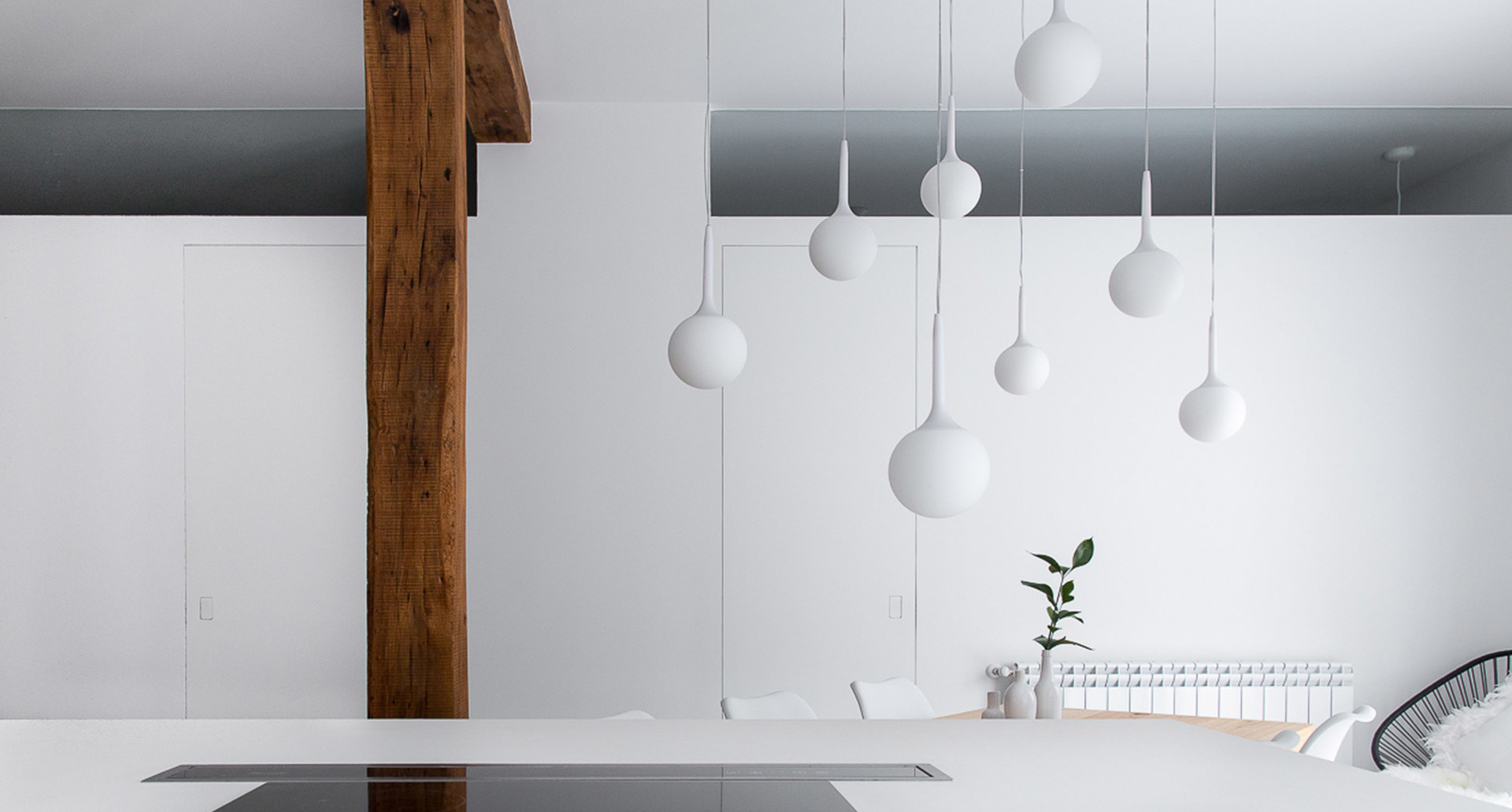 Cluster of white pendant lamps with spherical globes and teardrop shapes hanging at varying heights in a minimalist white interior
