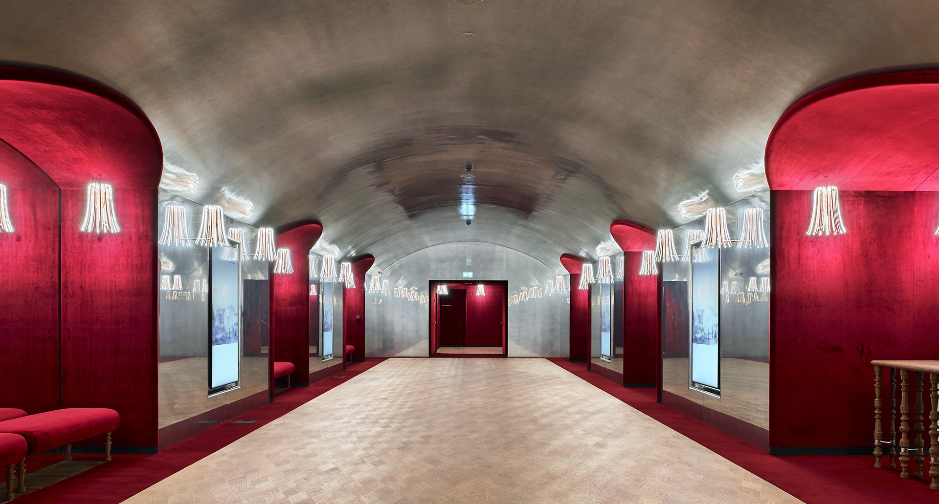 Elegant vaulted corridor with crimson red walls, mirrors, and Artemide wall sconces with white shades lining both sides.
