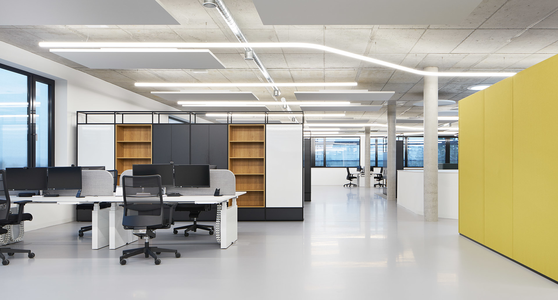 Modern open-plan office with Artemide linear LED ceiling lights illuminating workstations, shelving units, and yellow partition panels.