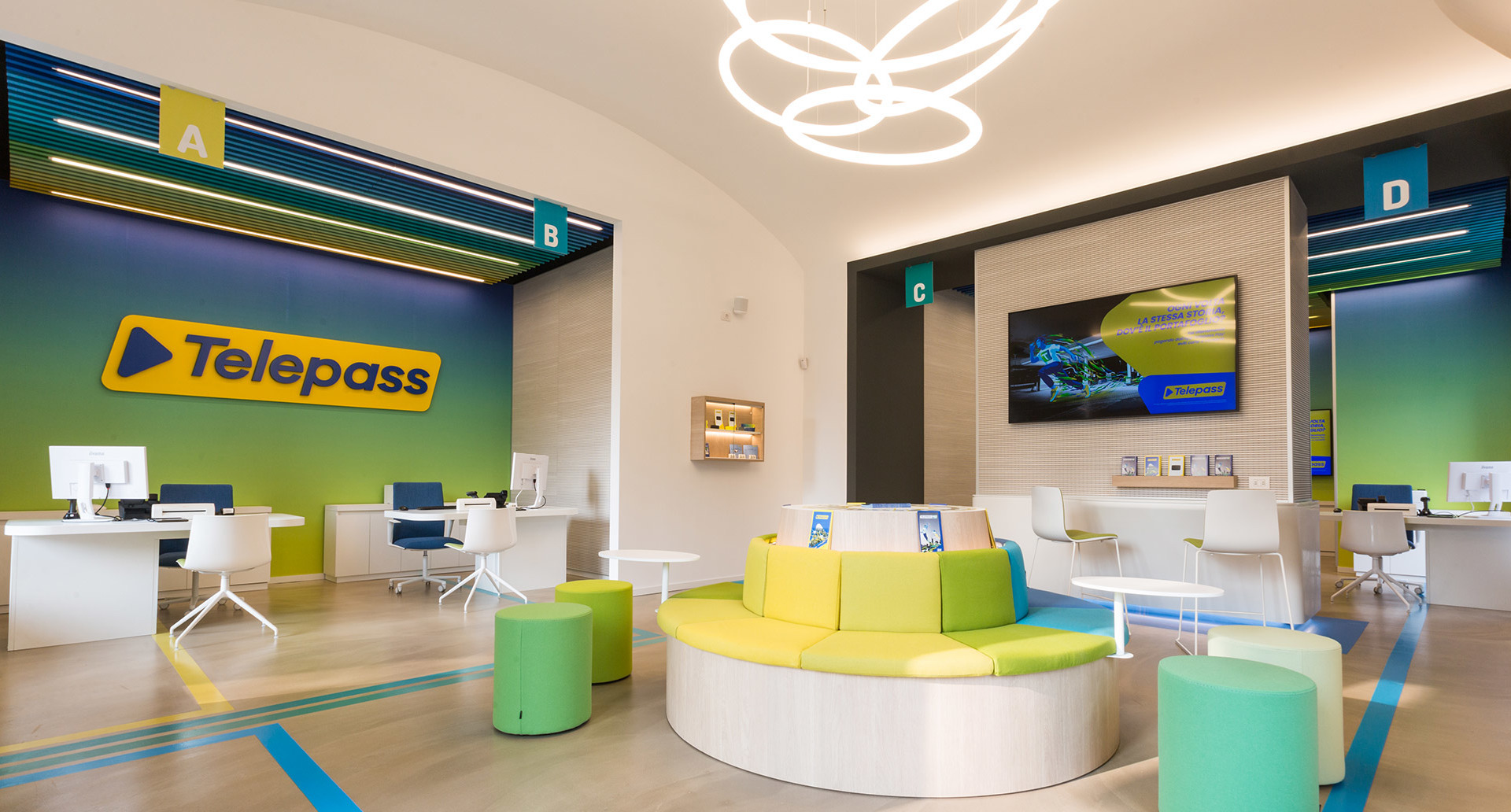 Telepass store interior with Artemide circular pendant lights illuminating a modern, colorful space with green and yellow seating areas.