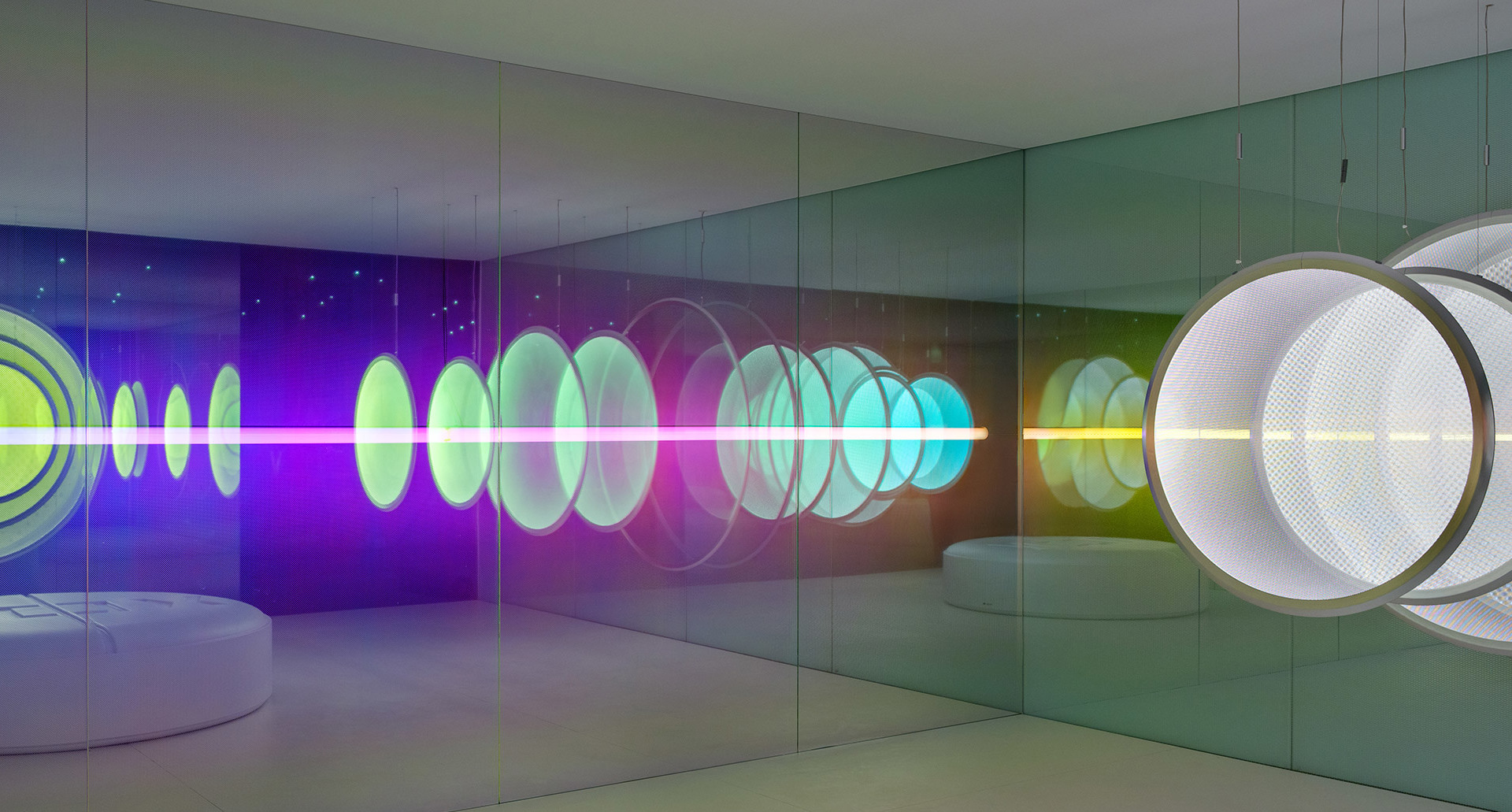 Immersive mirrored room with colorful neon light rings in purple, green, and cyan creating infinite reflections along the walls