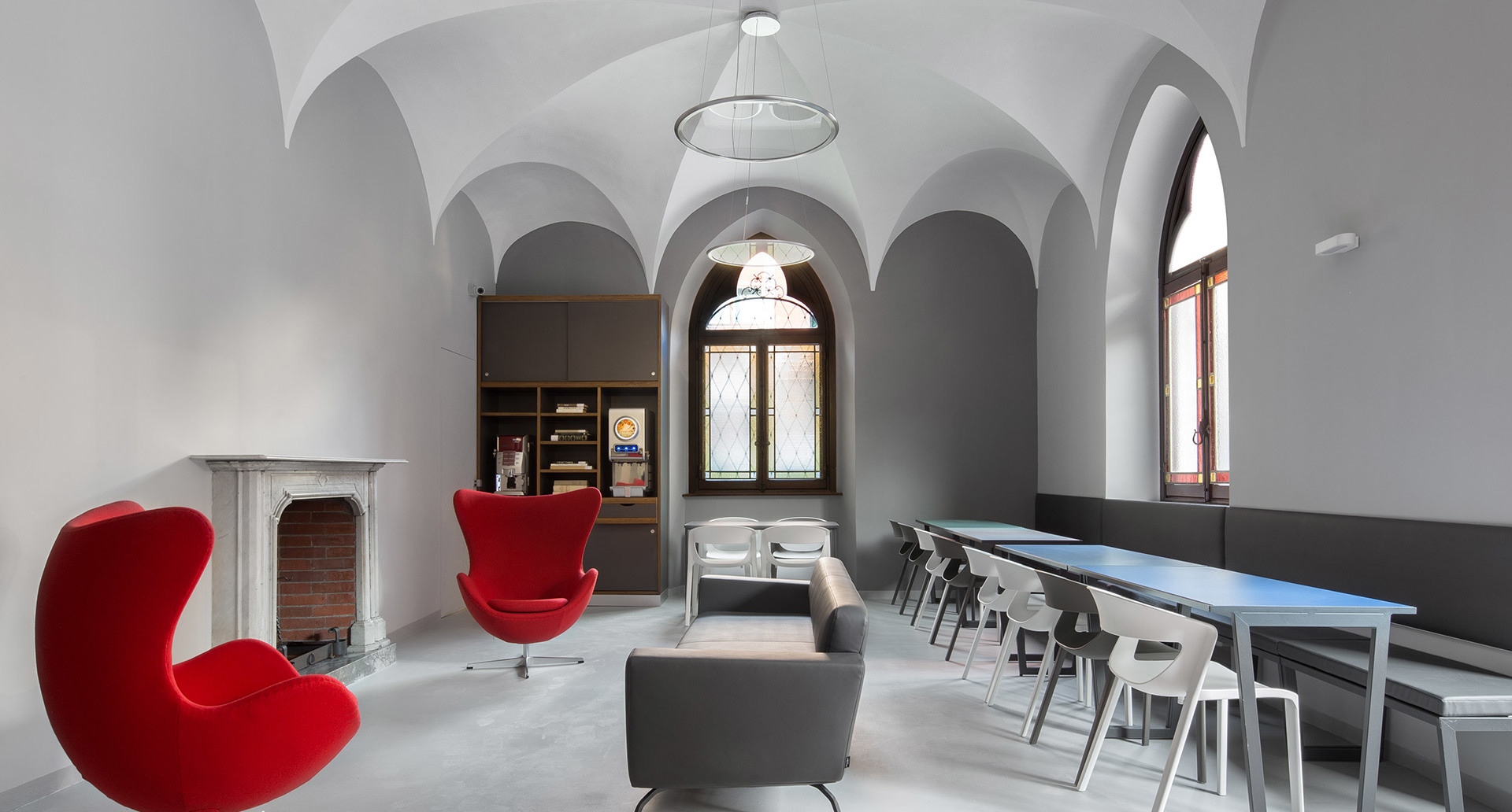 Vaulted room with Artemide pendant lamp over lounge area featuring red Egg chair, gray sofa, and long conference table with chairs