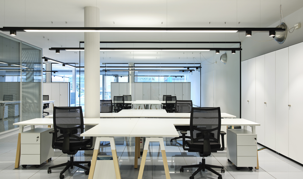 Modern open-plan office with white workstations, mesh chairs, and Artemide black track lighting system mounted on ceiling rails.