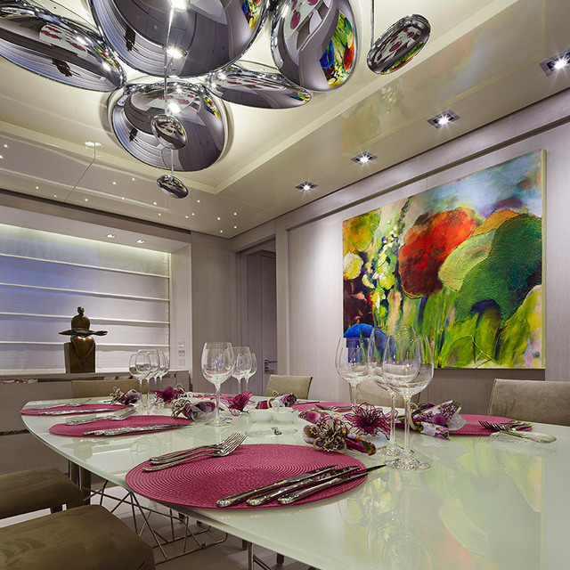 Elegant dining room with mirrored chrome pendant cluster ceiling light above a set table with magenta placemats and crystal glasses