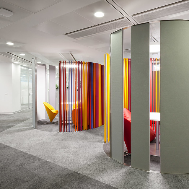 Modern office interior with colorful vertical rod partitions creating curved pods, recessed ceiling lights, and vibrant seating areas