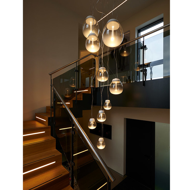 Multiple Artemide pendant lamps with oval glass diffusers cascade over a modern staircase, creating warm ambient lighting across two floors.