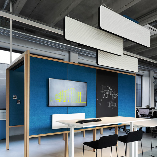 Artemide pendant acoustic panels with integrated lighting hang above a modern office workspace with blue partition walls and a monitor.