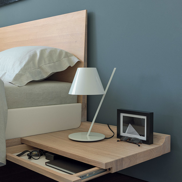Artemide white table lamp with angled stem and conical shade on a wooden bedside table in a modern bedroom