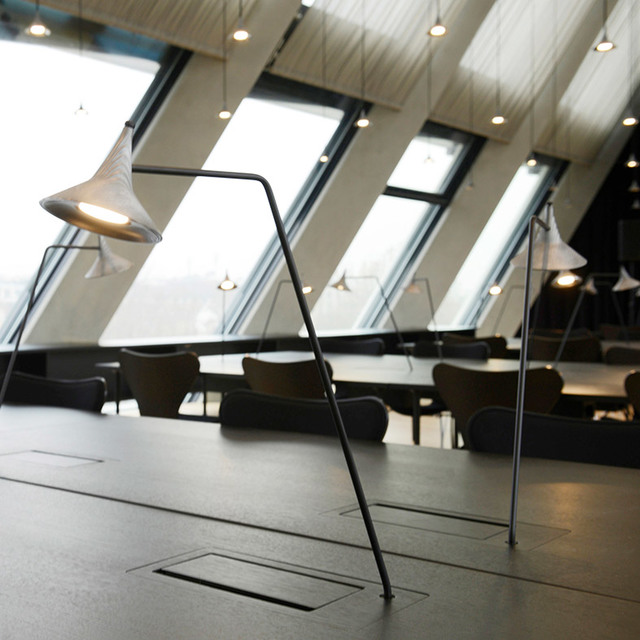 Artemide floor lamps with white conical shades on black angular frames illuminate a modern lounge area with large slanted windows.