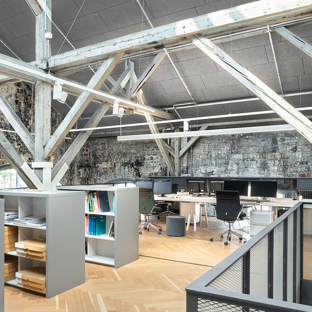 Industrial office space in converted building with exposed brick walls, wooden roof trusses, and linear pendant lights over workstations