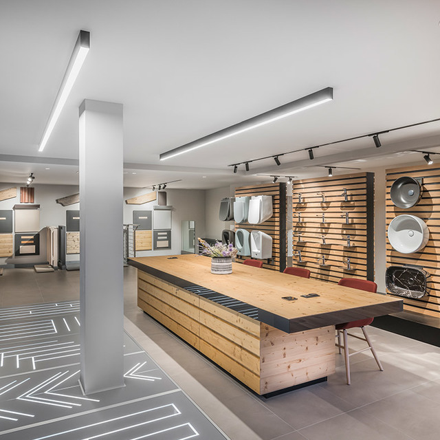 Showroom interior with Artemide linear LED ceiling fixtures and track lights illuminating a wooden central desk and product display wall.