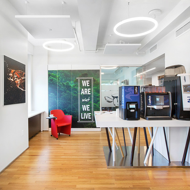 Modern office breakroom with two Artemide Alphabet of Light circular pendant lamps illuminating a coffee station and red armchair.