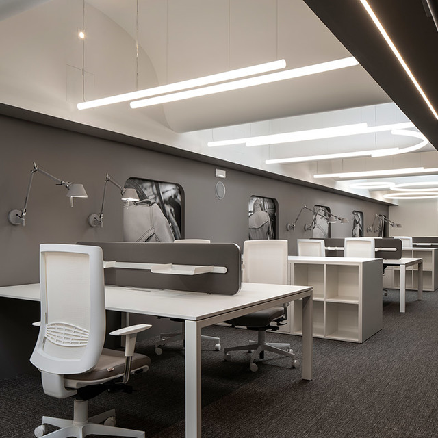Modern office with Artemide Tolomeo wall lamps and linear LED pendant lights illuminating white workstations with ergonomic chairs