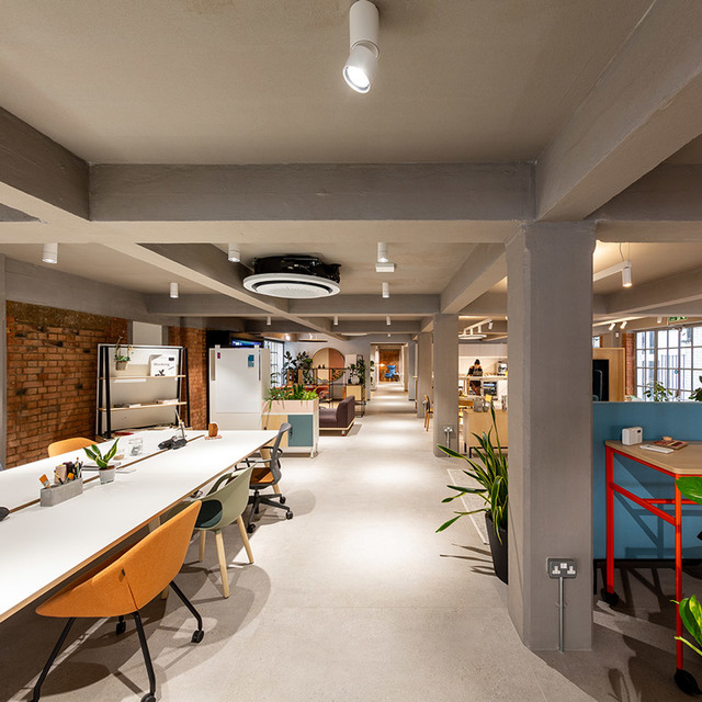 Modern open-plan office with Artemide ceiling spotlights and a circular pendant lamp illuminating long white desks and workstations.