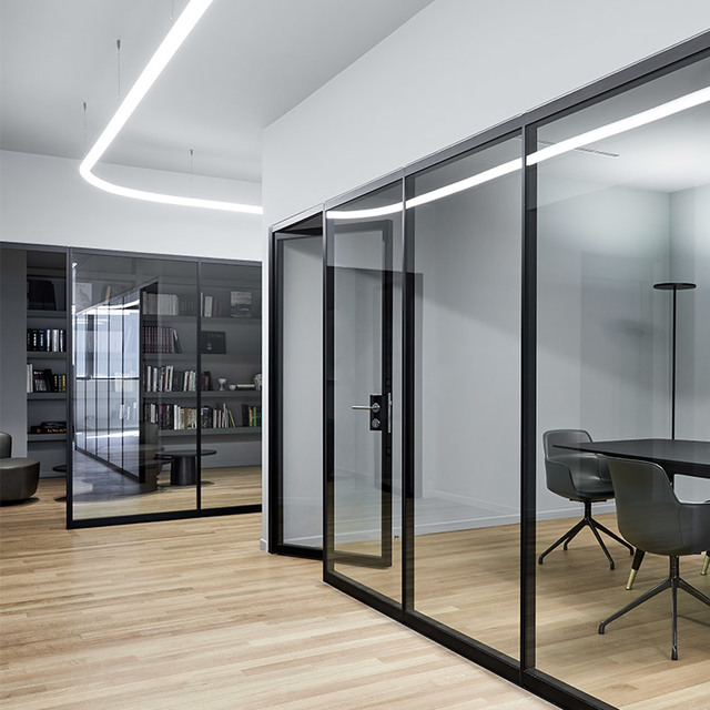 Modern office corridor with glass-partitioned meeting room, illuminated by curved linear LED ceiling lights on white walls and wood floor.