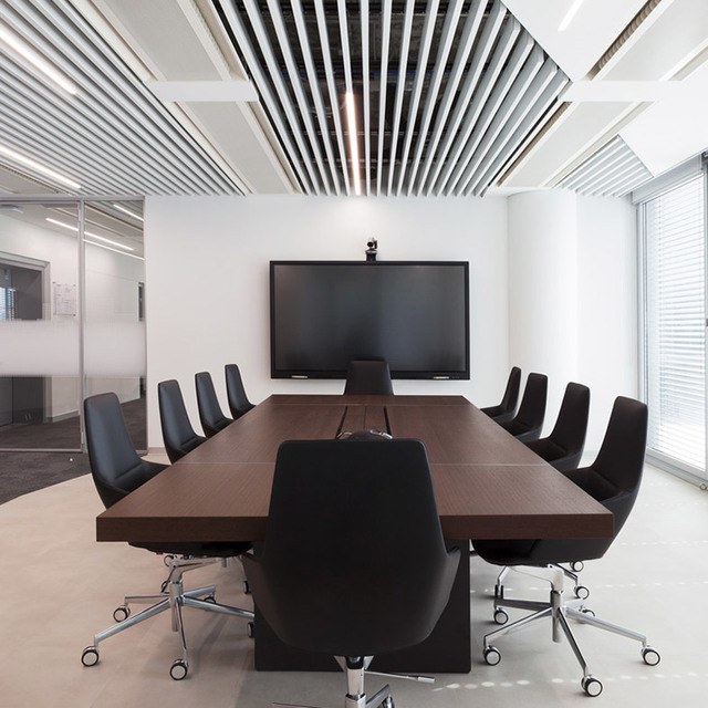 Modern conference room with dark wood table, black chairs, wall-mounted screen, and linear ceiling lighting system.