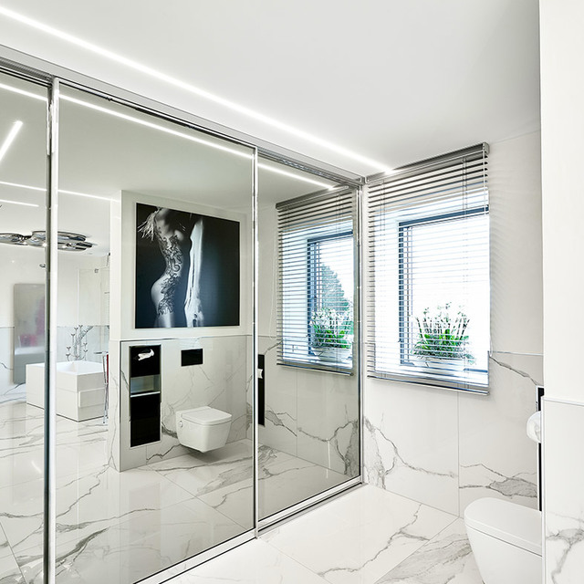 Modern white marble bathroom with glass partition, recessed linear LED ceiling light, venetian blinds, and wall-hung toilet