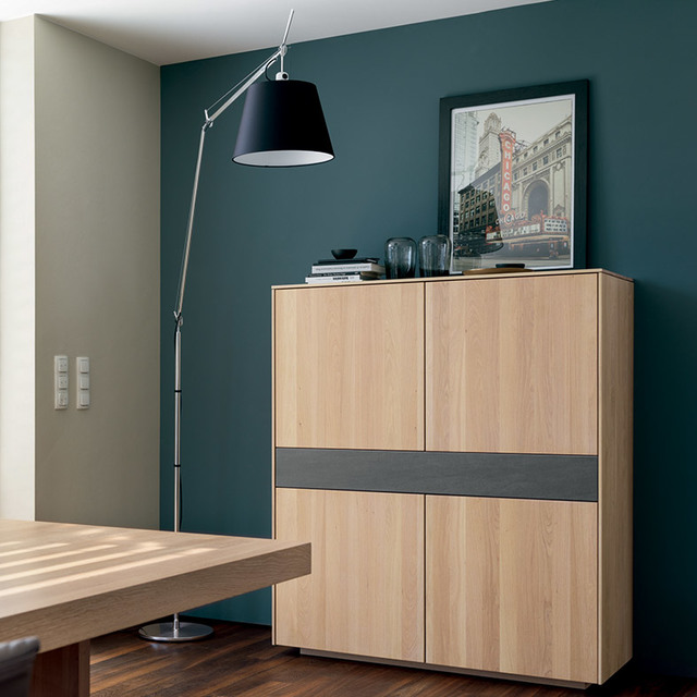 Artemide Tolomeo Mega floor lamp with black shade on adjustable arm, placed beside a wooden cabinet against a teal wall.