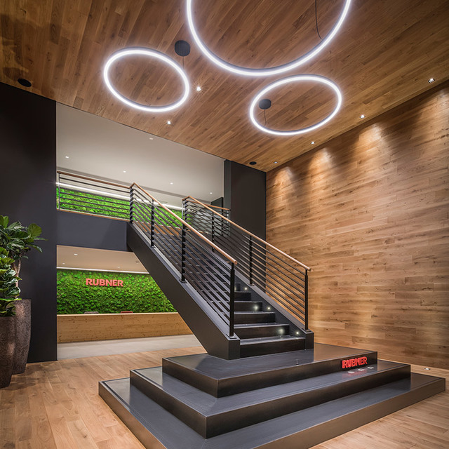 Rubner showroom entrance with circular LED pendant lights on wood ceiling, staircase, and green moss wall backdrop.