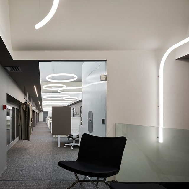 Modern office with Artemide curved LED strip lights on ceiling and walls, plus circular pendant rings illuminating an open workspace.