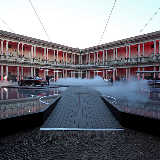 Artemide circular ring light installation over a misty walkway in a red-lit neoclassical courtyard at dusk