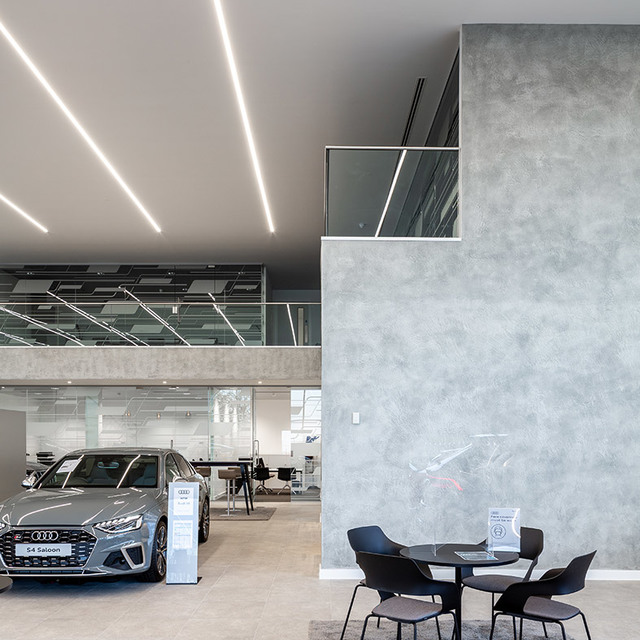 Audi showroom with recessed linear LED ceiling lights illuminating a grey A4 Saloon on display and a seating area.