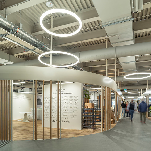 Retail space with Artemide Alphabet of Light circular pendant lamps illuminating a curved wooden display area with visitors.