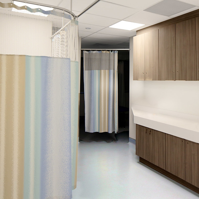 Hospital room corridor with privacy curtains on ceiling tracks, wood-finish cabinets, and recessed ceiling lighting panels.