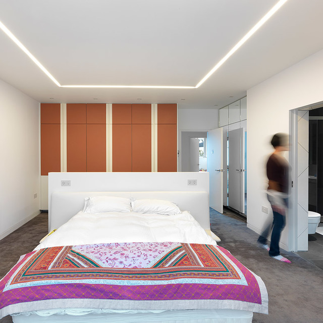 Modern bedroom with Artemide recessed LED linear ceiling lights forming a geometric pattern, illuminating a bed with colorful bedspread.