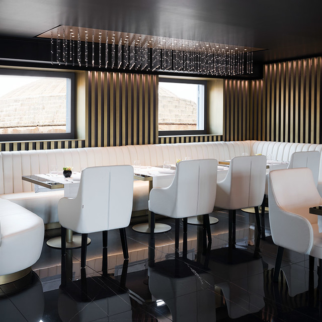 Elegant restaurant interior with white leather chairs, black tables, and a rectangular crystal pendant chandelier on a dark ceiling.