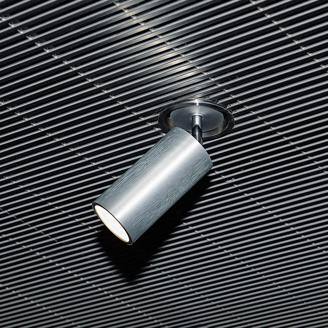Artemide recessed ceiling spotlight with adjustable brushed aluminum cylindrical head, mounted on a ribbed dark ceiling.
