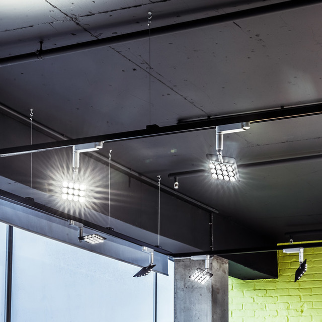 Multiple LED track and pendant spotlights with grid-pattern heads mounted on dark industrial ceiling, emitting bright white light.