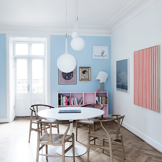 Dining room with two white spherical pendant lights above a round white table surrounded by wooden wishbone chairs, light blue walls