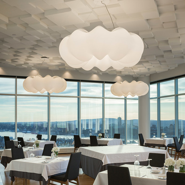 Restaurant interior with three Artemide Nebula pendant lamps resembling white clouds, hanging above elegantly set dining tables with city views.