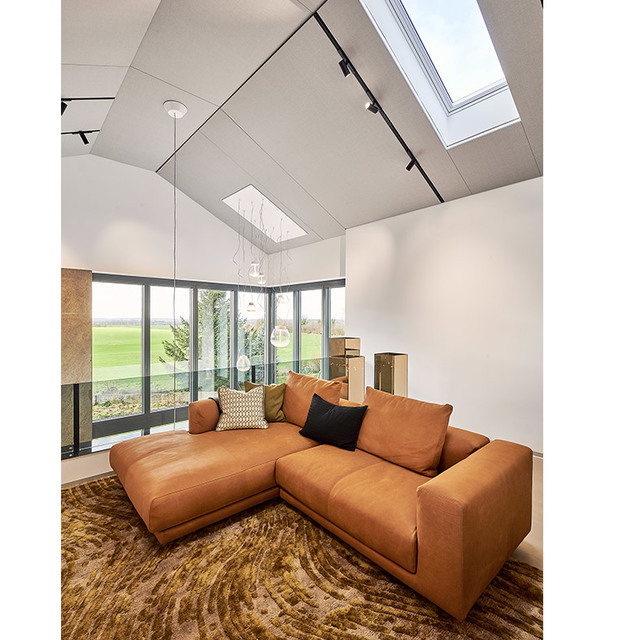 Modern living room with vaulted ceiling, track lighting, glass globe pendants, skylights, tan leather sectional sofa, and floor-to-ceiling windows.