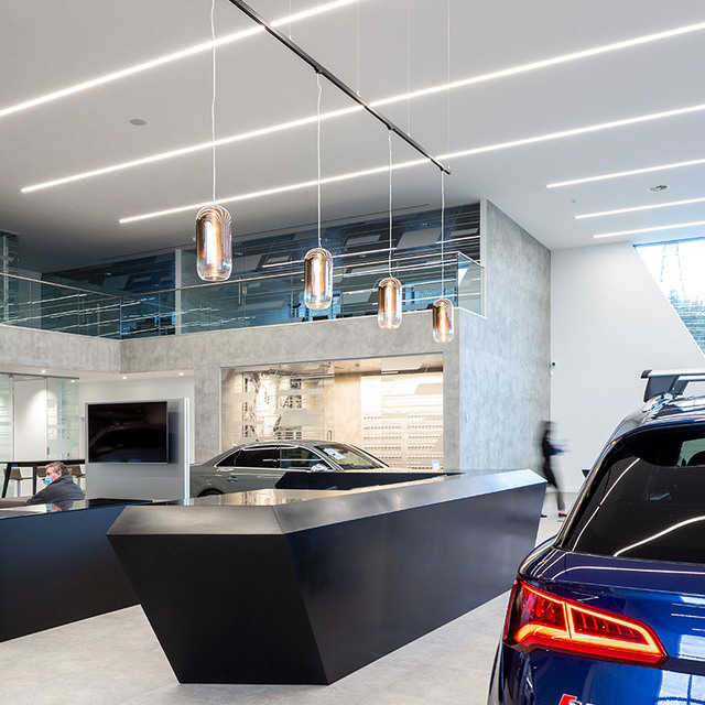 Car showroom with Artemide Nula pendant lamps in amber glass hanging over a dark angular reception desk, with linear ceiling lights.